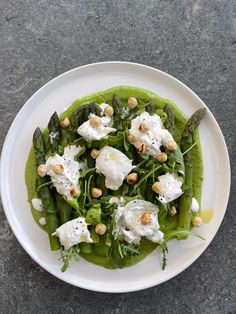 a white plate topped with asparagus and poached eggs on top of greens