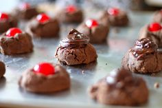 chocolate cookies with red candy on top sit on a cookie sheet