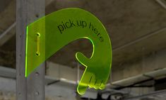 a green sign that says pick up here hanging from the side of a metal pole