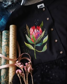 a shirt with a flower painted on it next to rolled up wrapping paper and flowers