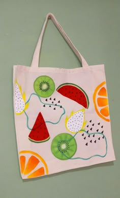 a white bag with fruit on it hanging from the wall next to a green wall