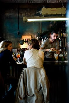 two people are sitting at a bar and one person is standing in front of the bar