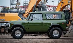 an old green truck parked in front of construction equipment