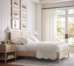 a bed with white sheets and pillows in a bedroom next to a large window that has pictures on the wall