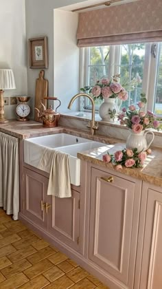 a kitchen with pink cabinets and flowers in vases on the window sill above the sink