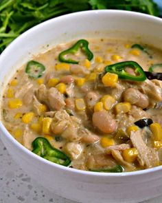 a white bowl filled with chicken and corn soup on top of a table next to some vegetables