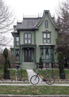 a bicycle is parked in front of a green victorian style house on a street corner