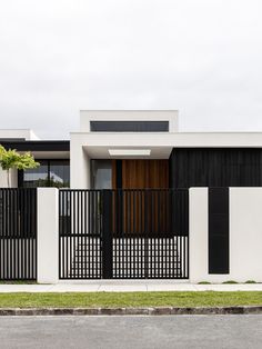 a modern house with black and white fences on the side of the street in front of it