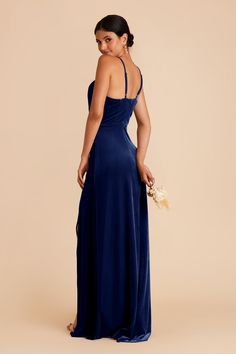 a woman in a long blue dress is looking back at the camera and she has her hand on her hip