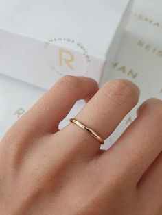 a woman's hand with a gold ring on her finger and a white box in the background