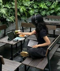 a woman sitting at a table eating food with headphones on her ears and using a laptop