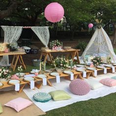 an outdoor picnic setting with pink and green decorations on the table, pillows, plates and other items