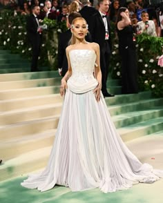 a woman in a white dress standing on steps with people behind her and taking pictures