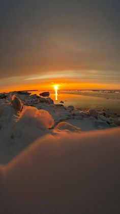 the sun is setting over some ice covered rocks and water with snow on it's sides