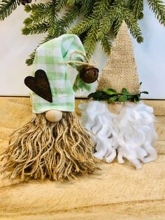 two christmas decorations are sitting next to each other on a wooden table with pine cones and evergreen branches