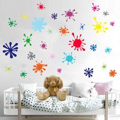 a teddy bear sitting on top of a bed next to a wall with paint splatters