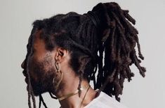 a man with dreadlocks wearing a white t - shirt and gold hoop earrings