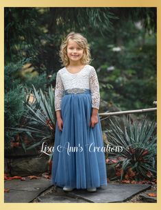 Dusty Blue Tulle Flower Girl Dress in Long Sleeves Fairytales do come true in our Full Length Lace Back Dress by Lisa Ann's Creations. This classic design is so sweet, featuring a low back lace bodice with scalloped edges and a layered tulle skirt that is extra full and dreamy. Ideal for that pretty flower girl dress, birthday party dress or special occasion. Our whimsical boho style special occasion dresses are the perfect choice for your little princess. Dress Features A soft white bodice, mad Dusty Blue Flower Girl Dress, Dusty Blue Toddler Dress, Dusty Blue Flower Girl Dress Boho, Junior Bridesmaid Dresses Dusty Blue, Dusty Blue Dress, Lace Back Dresses, Long Flower Girl Dresses, Flower Girl Dresses Blue, Layered Tulle Skirt