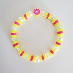 a yellow and pink beaded bracelet with an orange slice on the end, sitting on a white surface