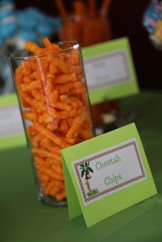 a glass filled with cheetos sitting on top of a table next to a sign