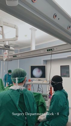 three surgeons in green scrubs are operating on the monitor and looking at an x - ray