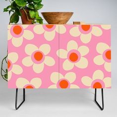 a pink cabinet with yellow and white flowers on it, next to a potted plant