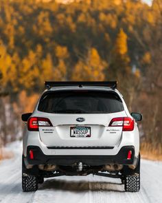 the back end of a white subarunt driving on a snowy road with trees in the background