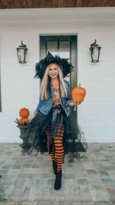 a woman dressed up as a witch standing in front of a house with pumpkins