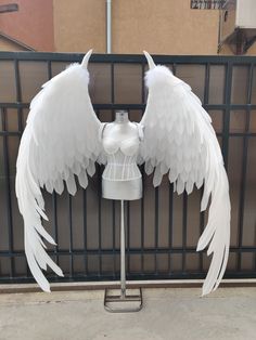 an angel wings on top of a mannequin's head in front of a fence