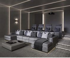 an empty theater room with grey couches and gray pillows on the seats is lit by recessed lights