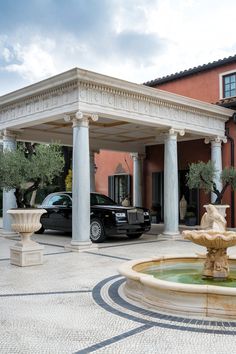 a black car is parked in front of a building with columns and a water fountain