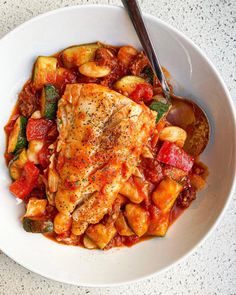 a white bowl filled with chicken and vegetables on top of a table next to a spoon