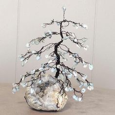 a small tree made out of wire and glass beads sitting on a table next to a rock