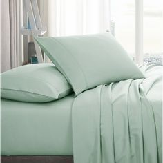 a bed covered in light green sheets and pillows