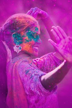 a woman covered in purple and blue powder holding her hands out to the side,