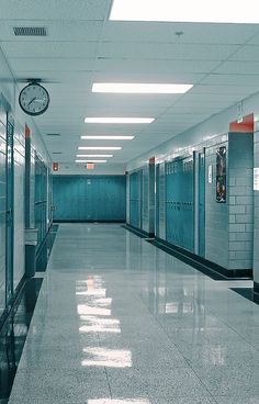 an empty hallway with blue lockers and a clock hanging from the ceiling in front of it