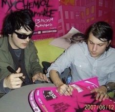 two young men sitting at a table looking at something on a pink book with writing on it