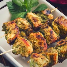 several skewers of meat and vegetables on a white plate with mint garnish