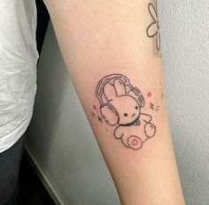 a small tattoo on the arm of a girl with headphones and a teddy bear