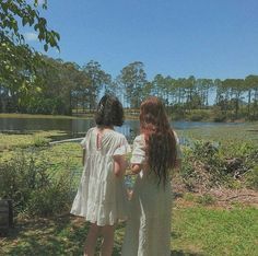 two women standing next to each other in front of a lake