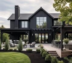 a large black house with lots of windows and patio furniture in front of the house