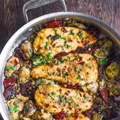 a pan filled with chicken and vegetables on top of a wooden table