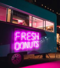 a neon sign that reads fresh donuts on the side of a food truck at night