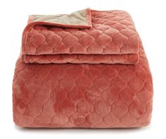 a blanket that is laying on top of a white surface with a light brown pillow behind it