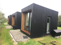 three black cabins with wooden doors and windows on the side of a grass covered field