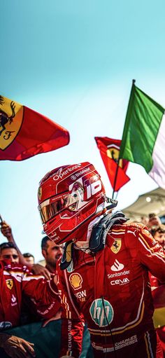 a man in a racing suit and helmet walking through a crowd with flags behind him