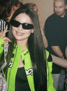 a woman wearing sunglasses and a neon green jacket at a party with other people in the background