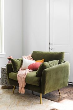 a green couch with pillows on it in front of a white wall and wooden floor