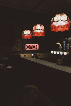 an open sign is lit up in the dark with three lamps hanging above it and on the wall