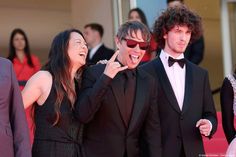 three people standing next to each other in front of a group of people on a red carpet